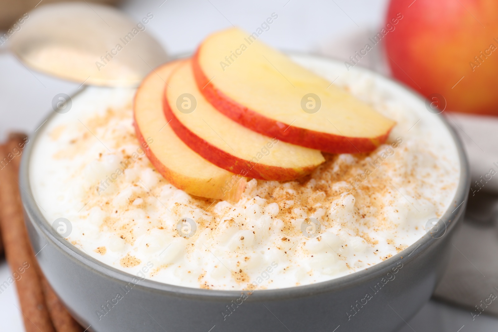 Photo of Delicious rice pudding with apples and cinnamon on white table, closeup