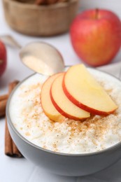 Photo of Delicious rice pudding with apples and cinnamon on white table, closeup