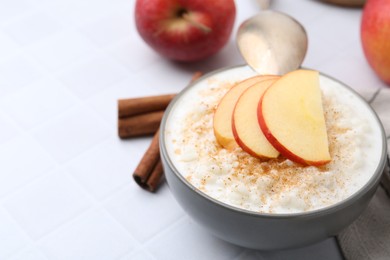 Photo of Delicious rice pudding with apples and cinnamon on white tiled table, closeup. Space for text