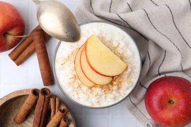 Photo of Delicious rice pudding with apples and cinnamon on white tiled table, flat lay