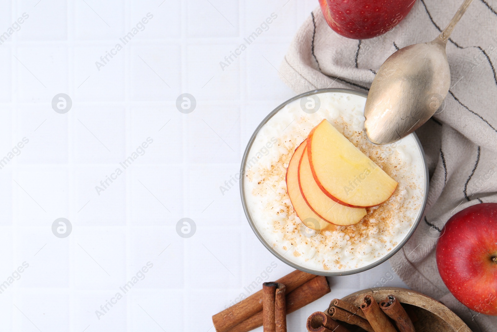 Photo of Delicious rice pudding with apples and cinnamon on white tiled table, flat lay. Space for text