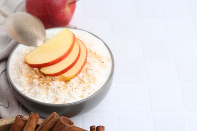 Photo of Delicious rice pudding with apples and cinnamon on white tiled table, closeup. Space for text