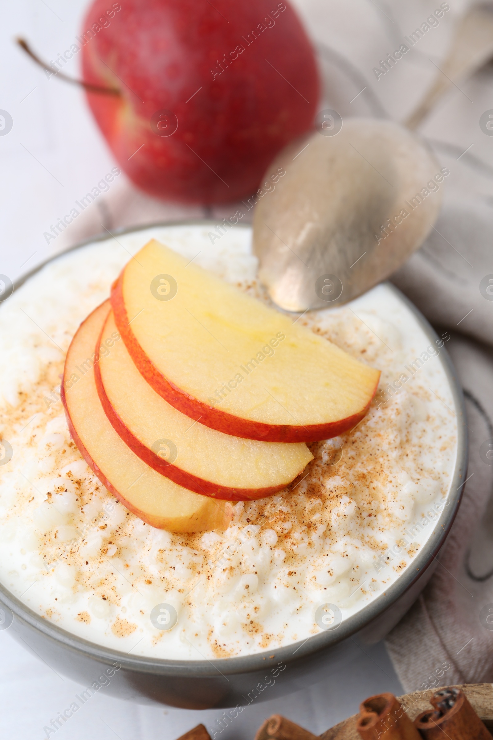 Photo of Delicious rice pudding with apples and cinnamon on white table, closeup