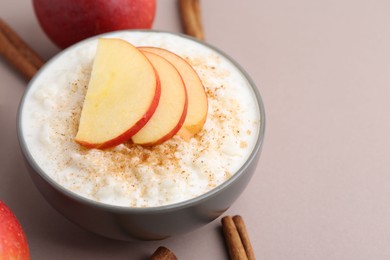 Photo of Delicious rice pudding with apples and cinnamon on color background, closeup. Space for text