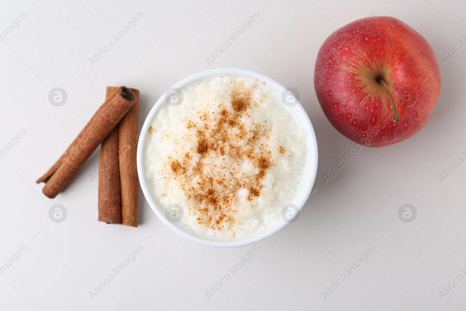 Photo of Delicious rice pudding with apple and cinnamon on light background, flat lay