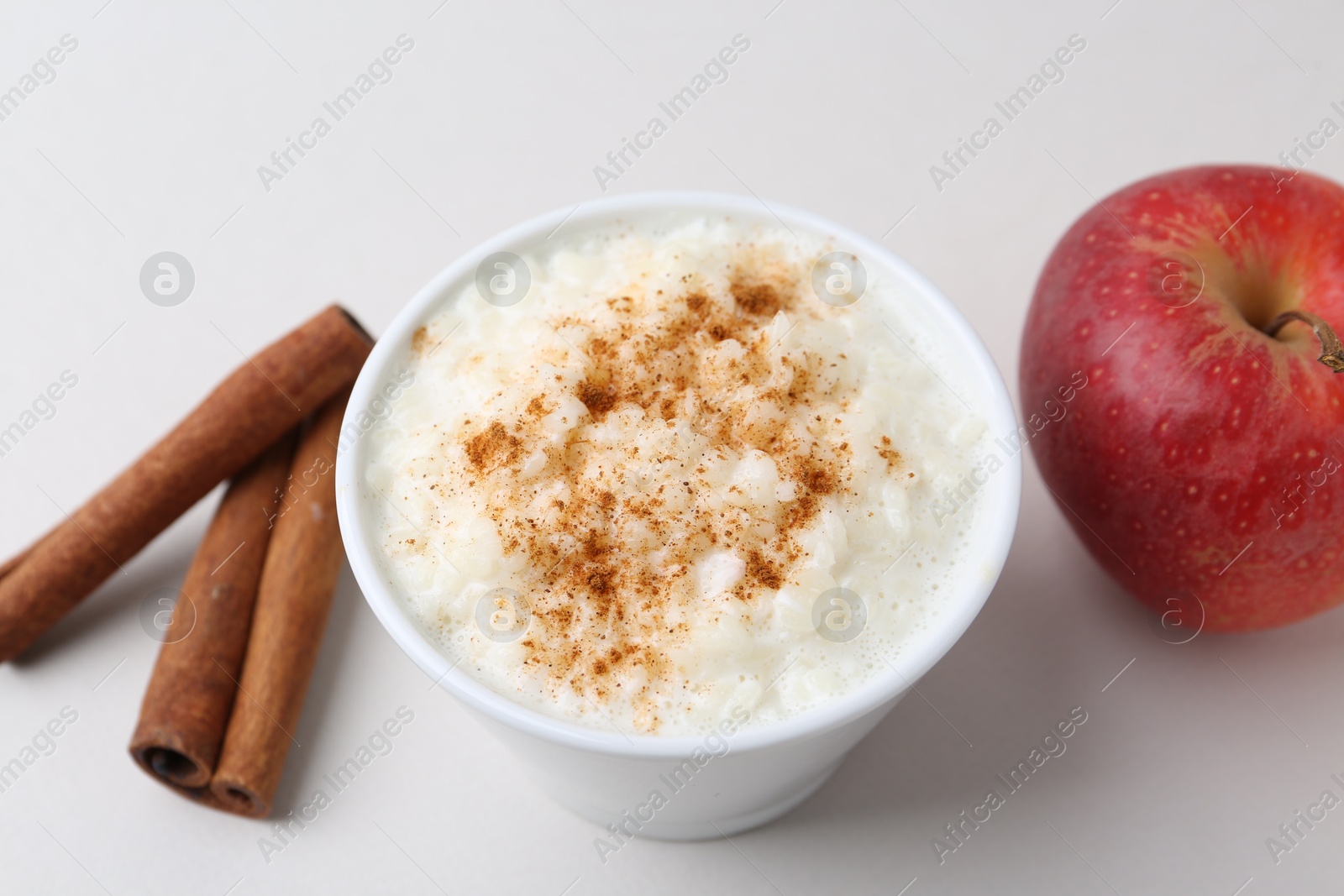 Photo of Delicious rice pudding with apple and cinnamon on light background, closeup