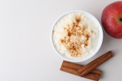 Photo of Delicious rice pudding with apple and cinnamon on light background, flat lay. Space for text