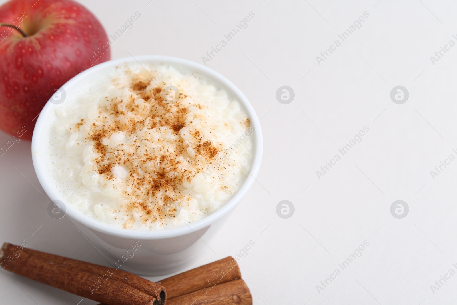 Photo of Delicious rice pudding with apple and cinnamon on light background, closeup. Space for text