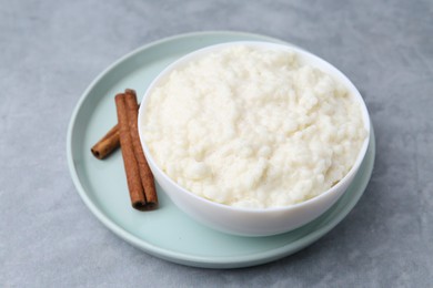 Photo of Delicious rice pudding with cinnamon sticks on grey table, closeup