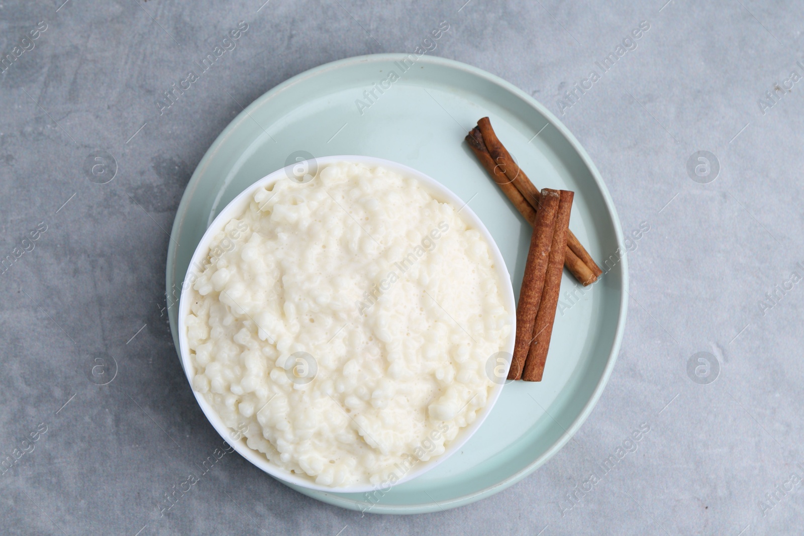 Photo of Delicious rice pudding with cinnamon sticks on grey table, top view