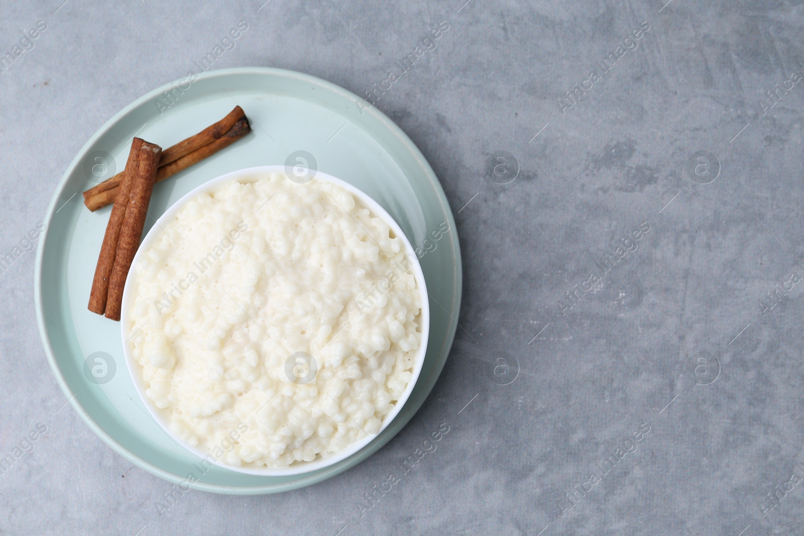 Photo of Delicious rice pudding with cinnamon sticks on grey table, top view. Space for text