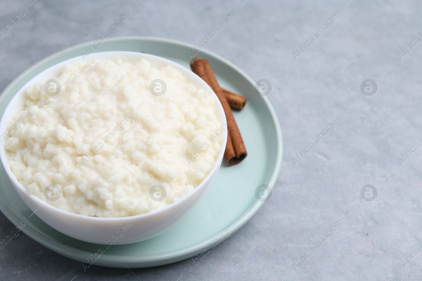 Photo of Delicious rice pudding with cinnamon sticks on grey table, closeup. Space for text