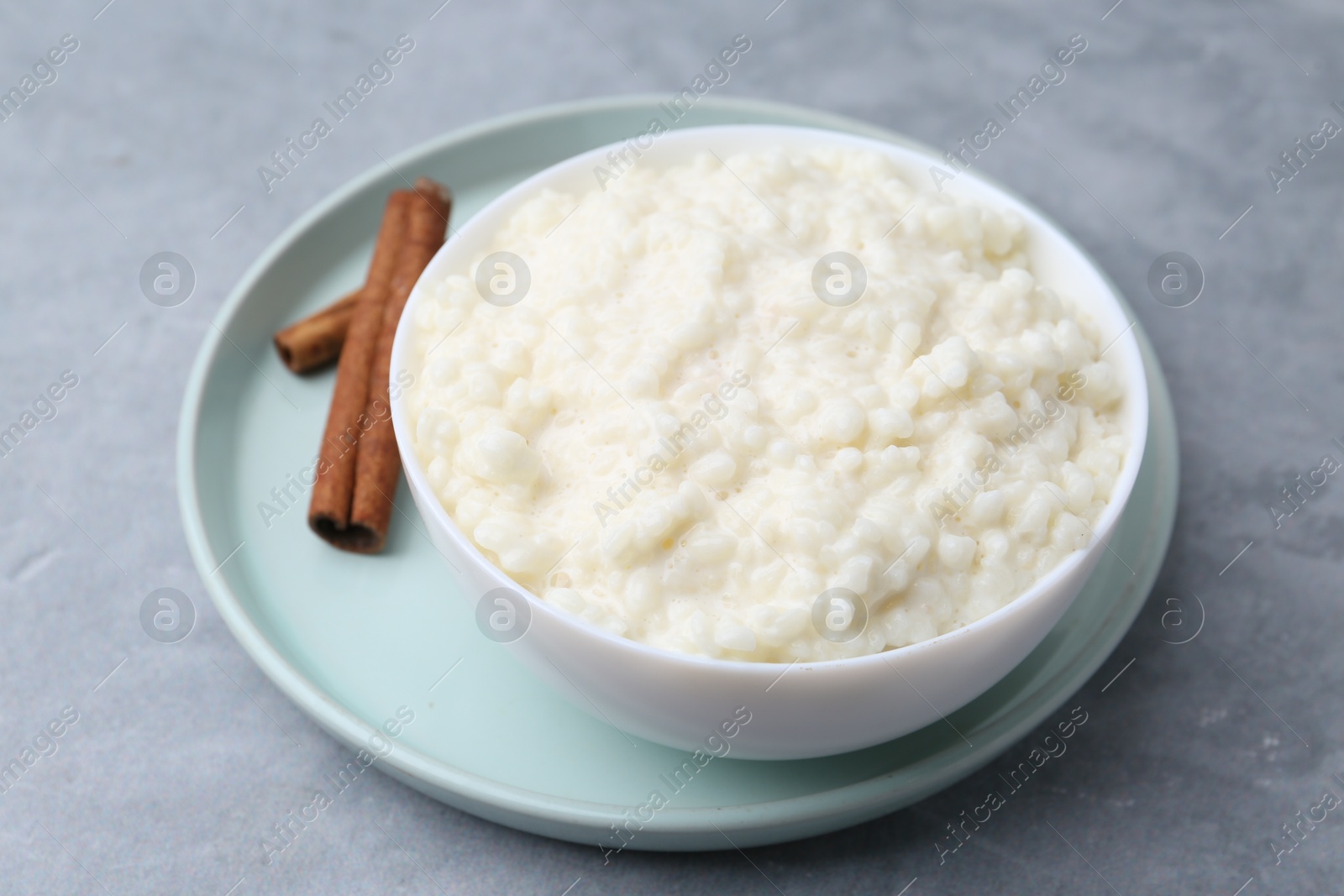 Photo of Delicious rice pudding with cinnamon sticks on grey table, closeup