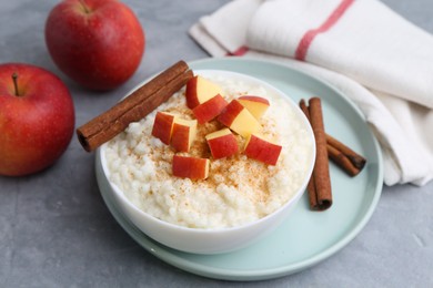 Photo of Delicious rice pudding with apples and cinnamon on grey table, closeup