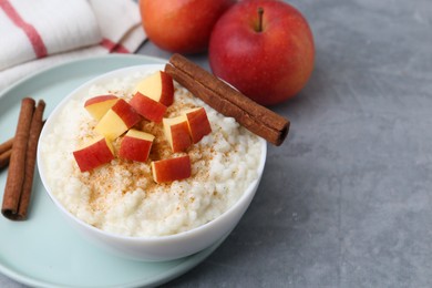 Photo of Delicious rice pudding with apples and cinnamon on grey table, closeup. Space for text