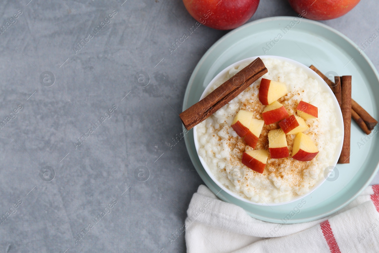 Photo of Delicious rice pudding with apples and cinnamon on grey table, flat lay. Space for text