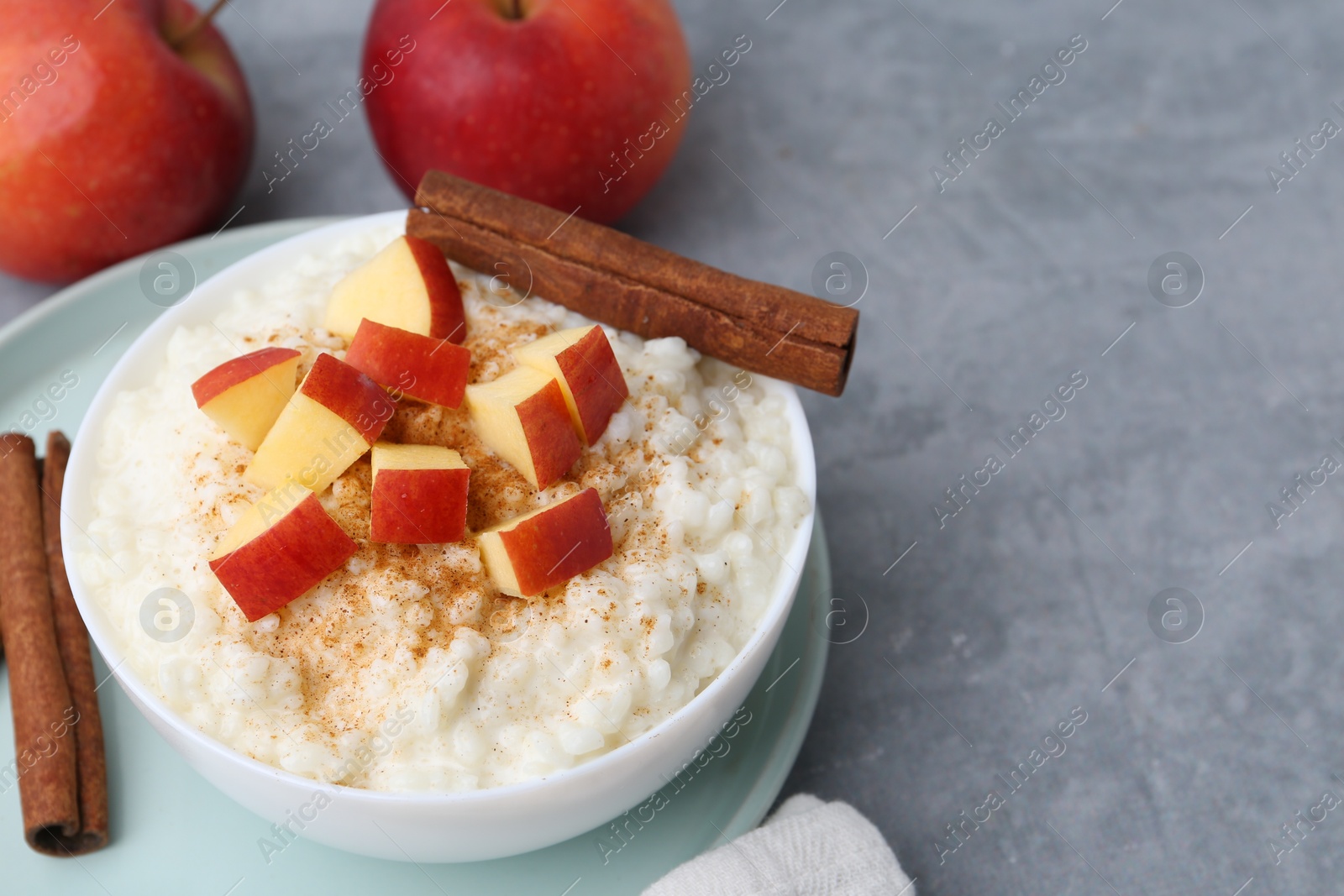 Photo of Delicious rice pudding with apples and cinnamon on grey table, closeup. Space for text