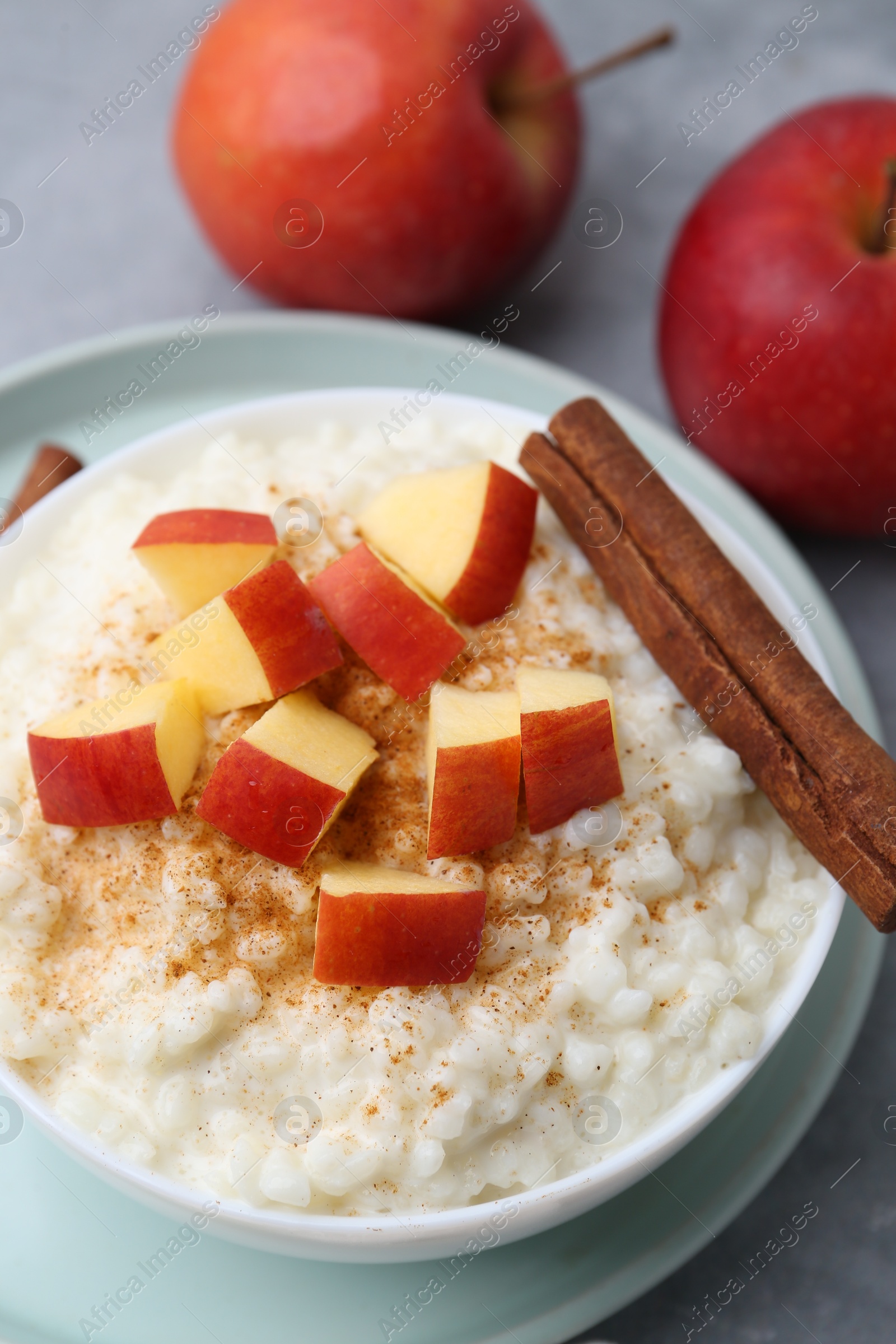 Photo of Delicious rice pudding with apples and cinnamon on grey table, closeup