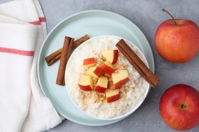 Photo of Delicious rice pudding with apples and cinnamon on grey table, flat lay