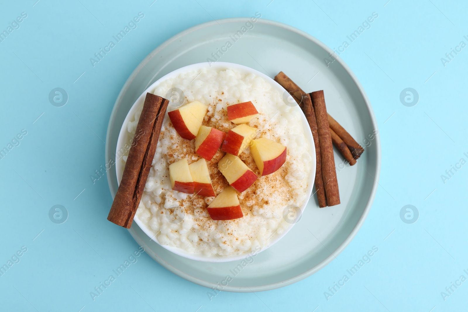 Photo of Delicious rice pudding with apples and cinnamon on light blue background, top view