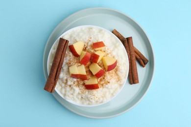 Photo of Delicious rice pudding with apples and cinnamon on light blue background, top view