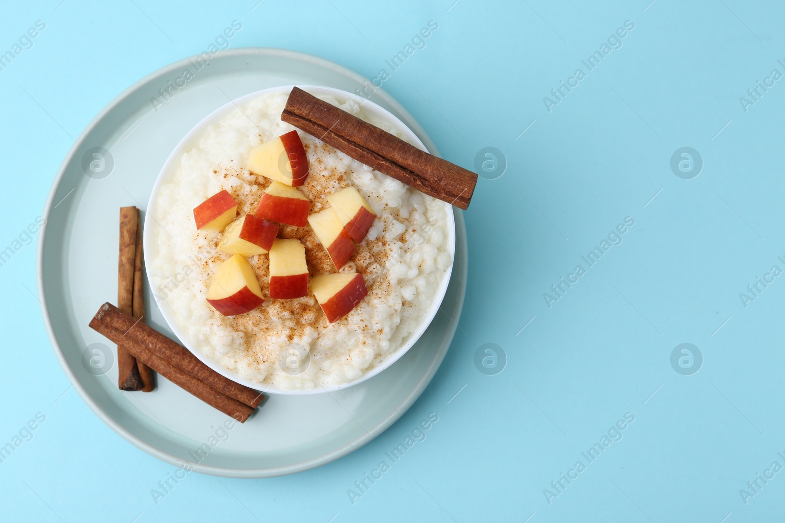 Photo of Delicious rice pudding with apples and cinnamon on light blue background, top view. Space for text