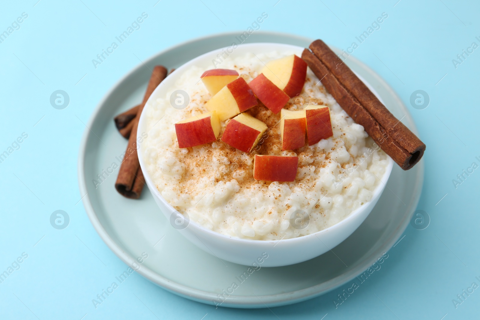 Photo of Delicious rice pudding with apples and cinnamon on light blue background, closeup