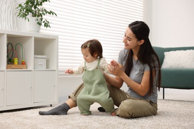 Photo of First steps. Mother supporting daughter while she learning to walk at home