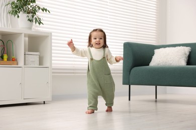 Photo of First steps. Cute little baby learning to walk at home