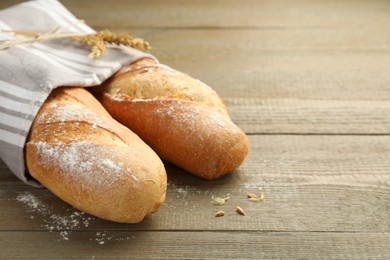 Photo of Freshly baked baguettes on wooden table, closeup. Space for text