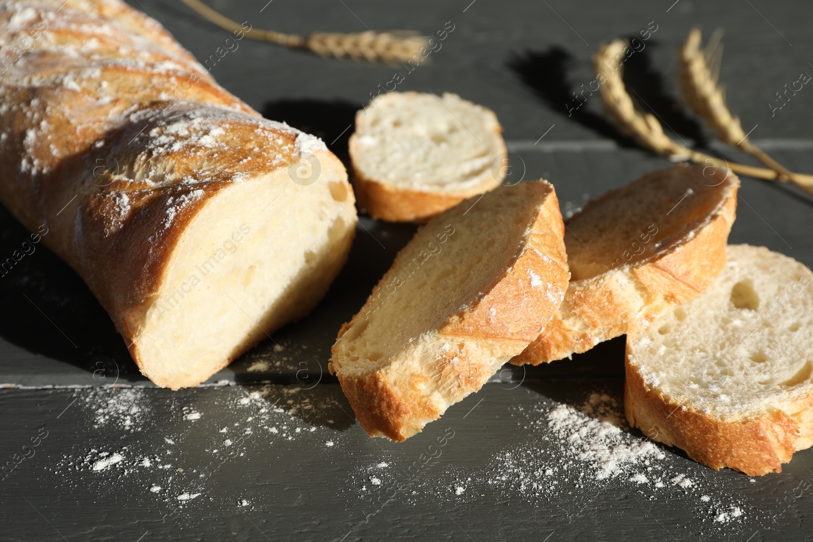 Photo of Pieces of fresh baguette with flour and spikes on grey wooden table