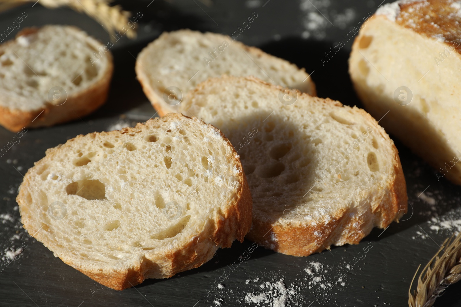 Photo of Pieces of fresh baguette with flour on grey wooden table, closeup