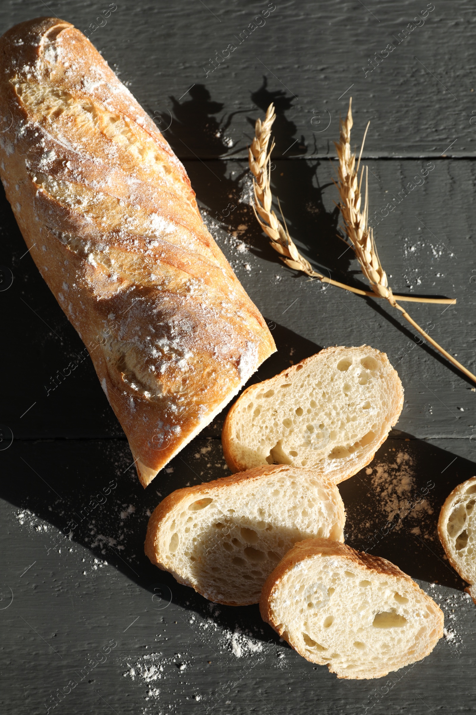 Photo of Pieces of fresh baguette with flour and spikes on grey wooden table, flat lay