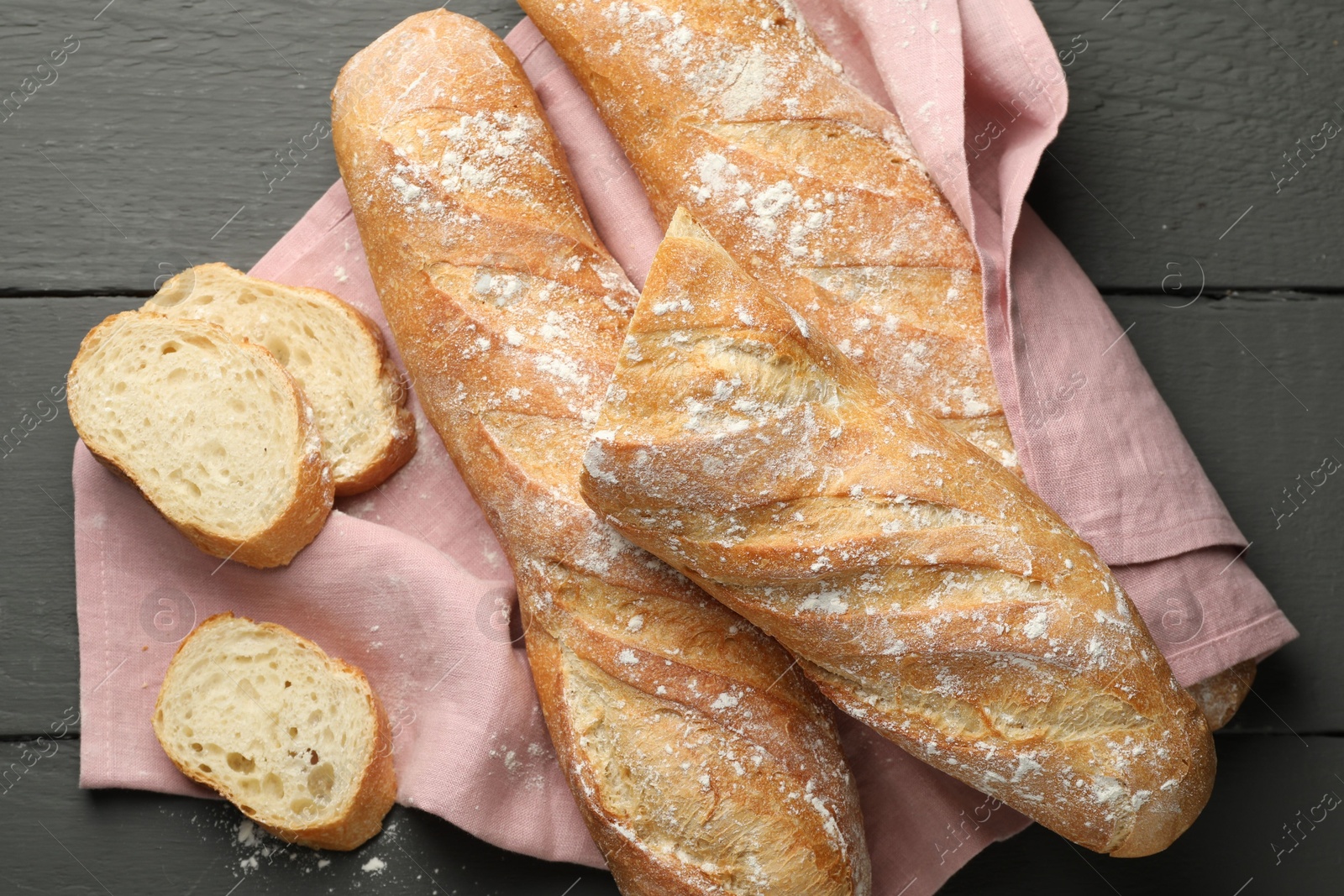 Photo of Cut fresh baguettes on grey wooden table, top view