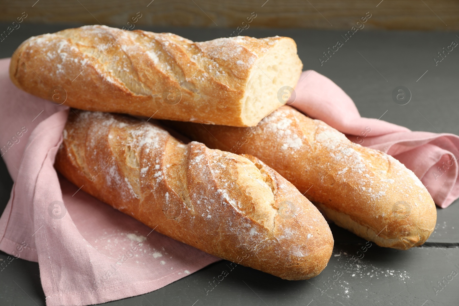 Photo of Cut fresh baguettes on grey wooden table, closeup