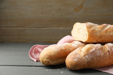 Cut fresh baguettes on grey wooden table, closeup. Space for text