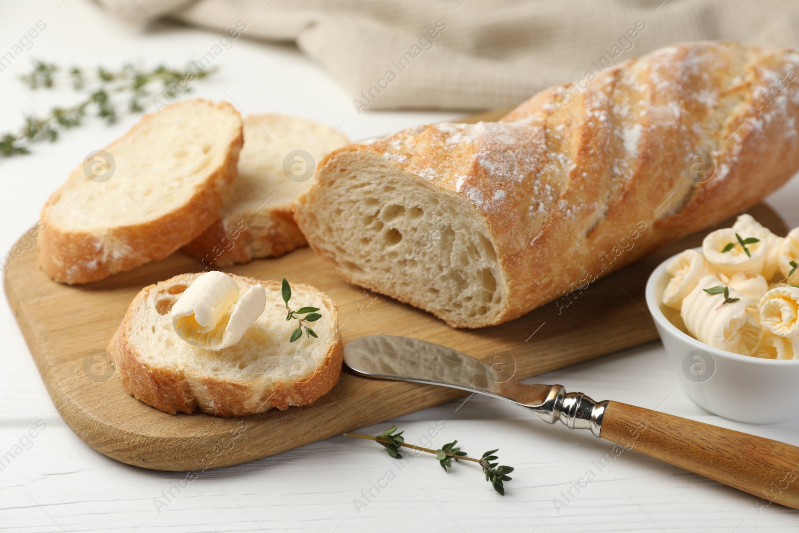 Photo of Cut baguette with butter and herbs on white wooden table, closeup