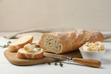 Photo of Cut baguette with butter and herbs on white wooden table