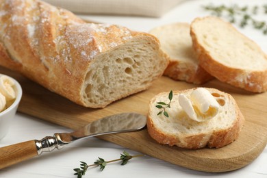 Photo of Cut baguette with butter and herbs on white wooden table, closeup