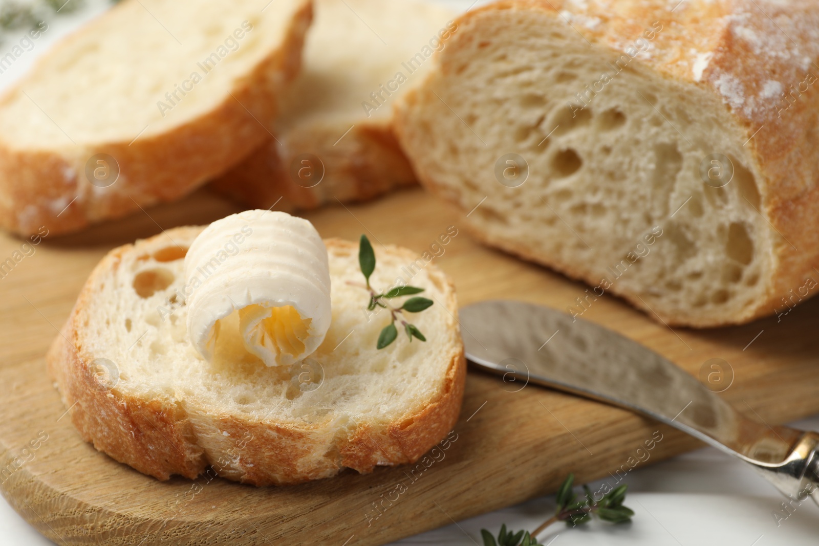 Photo of Cut baguette with butter and herbs on white wooden table, closeup