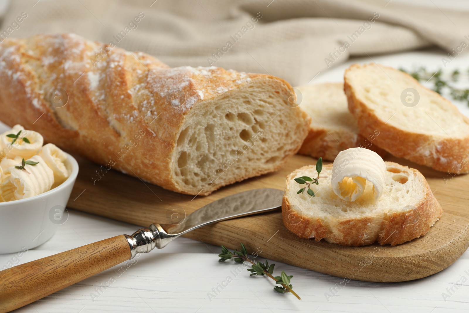 Photo of Cut baguette with butter and herbs on white wooden table, closeup