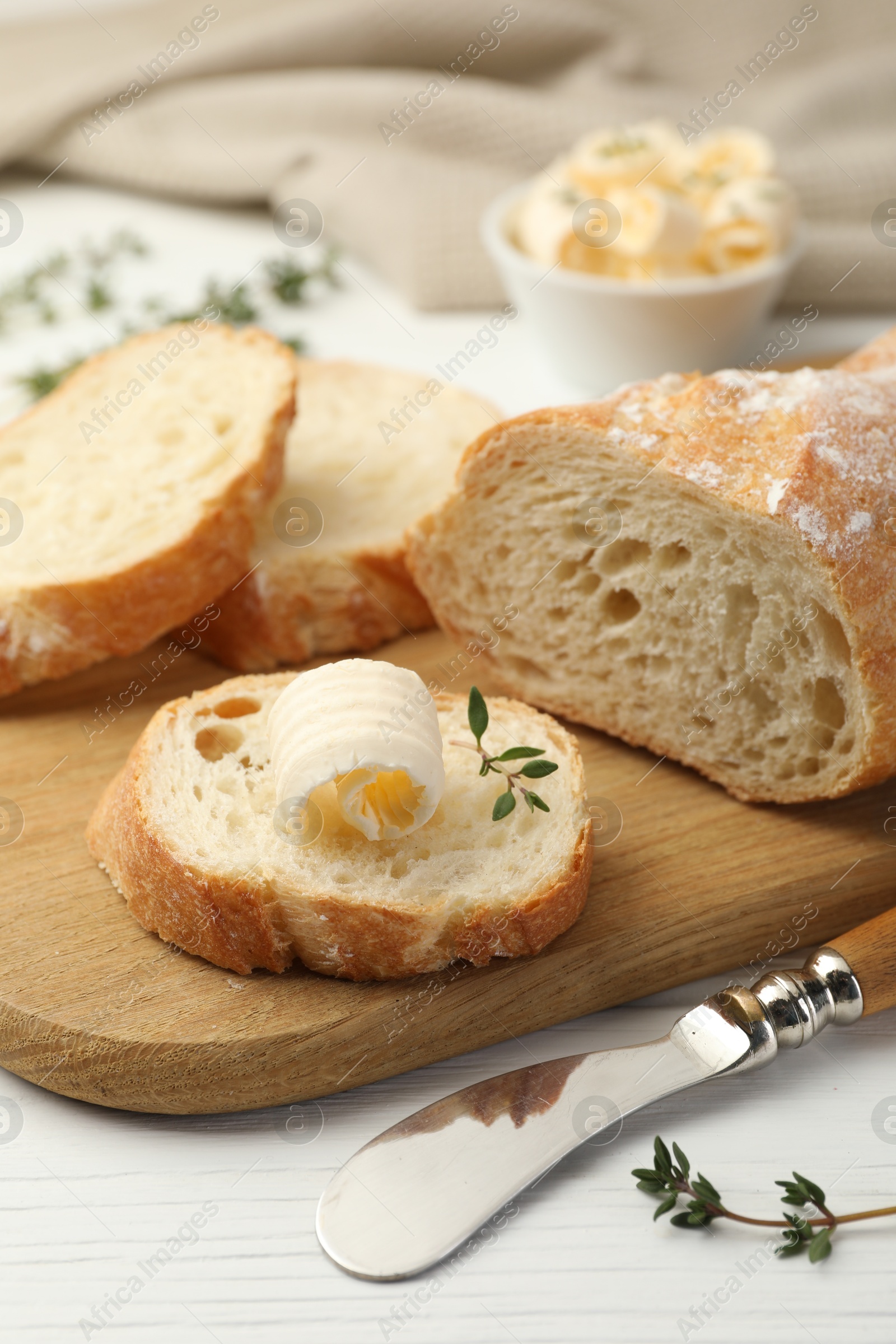 Photo of Cut baguette with butter and herbs on white wooden table, closeup