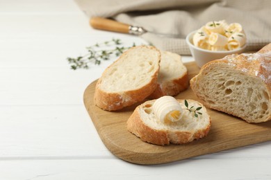 Photo of Cut baguette with butter and herbs on white wooden table, closeup