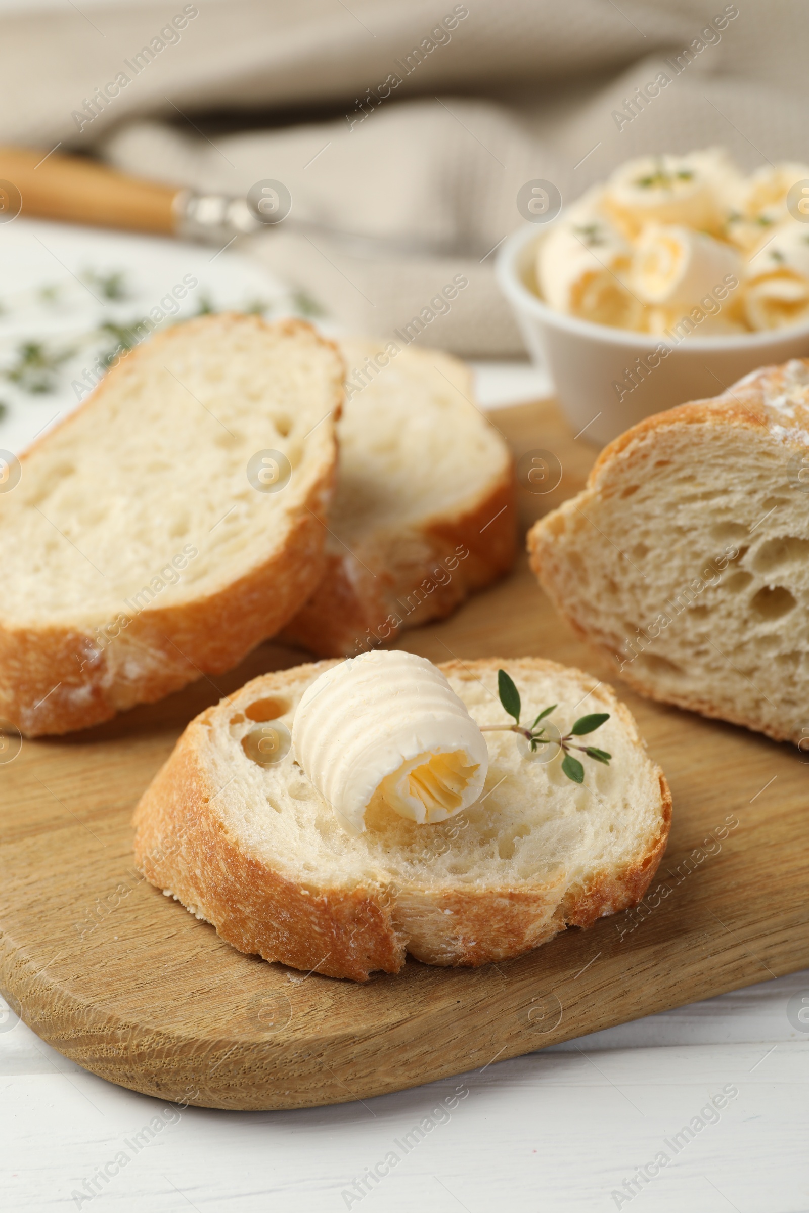 Photo of Cut baguette with butter and herbs on white wooden table, closeup