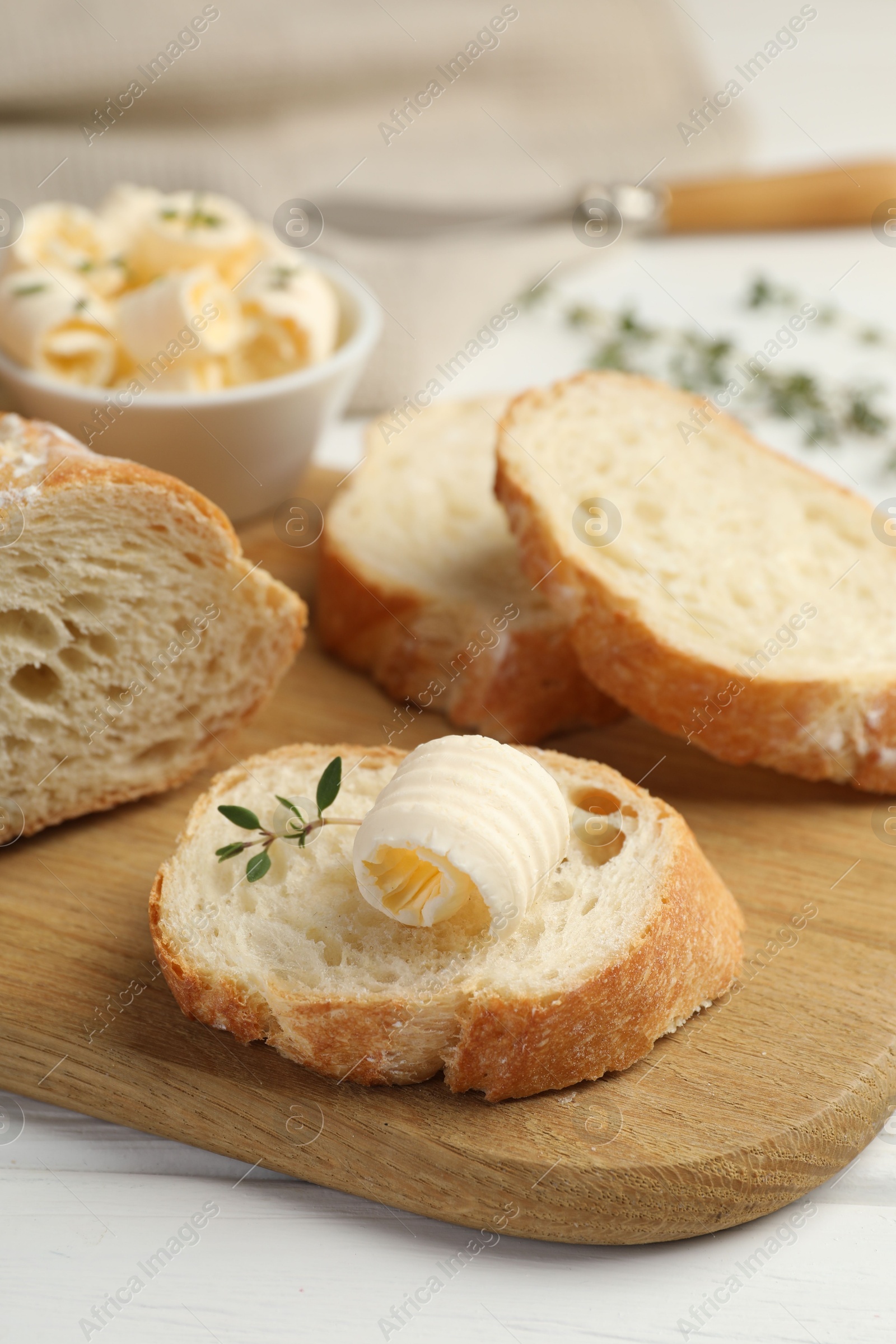 Photo of Cut baguette with butter and herbs on white wooden table, closeup