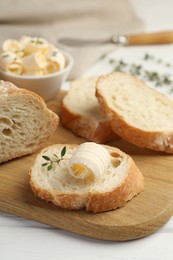 Photo of Cut baguette with butter and herbs on white wooden table, closeup