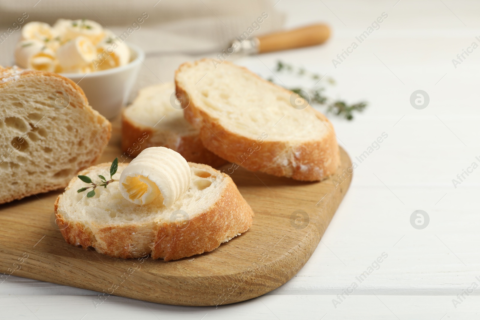 Photo of Cut baguette with butter and herbs on white wooden table, closeup