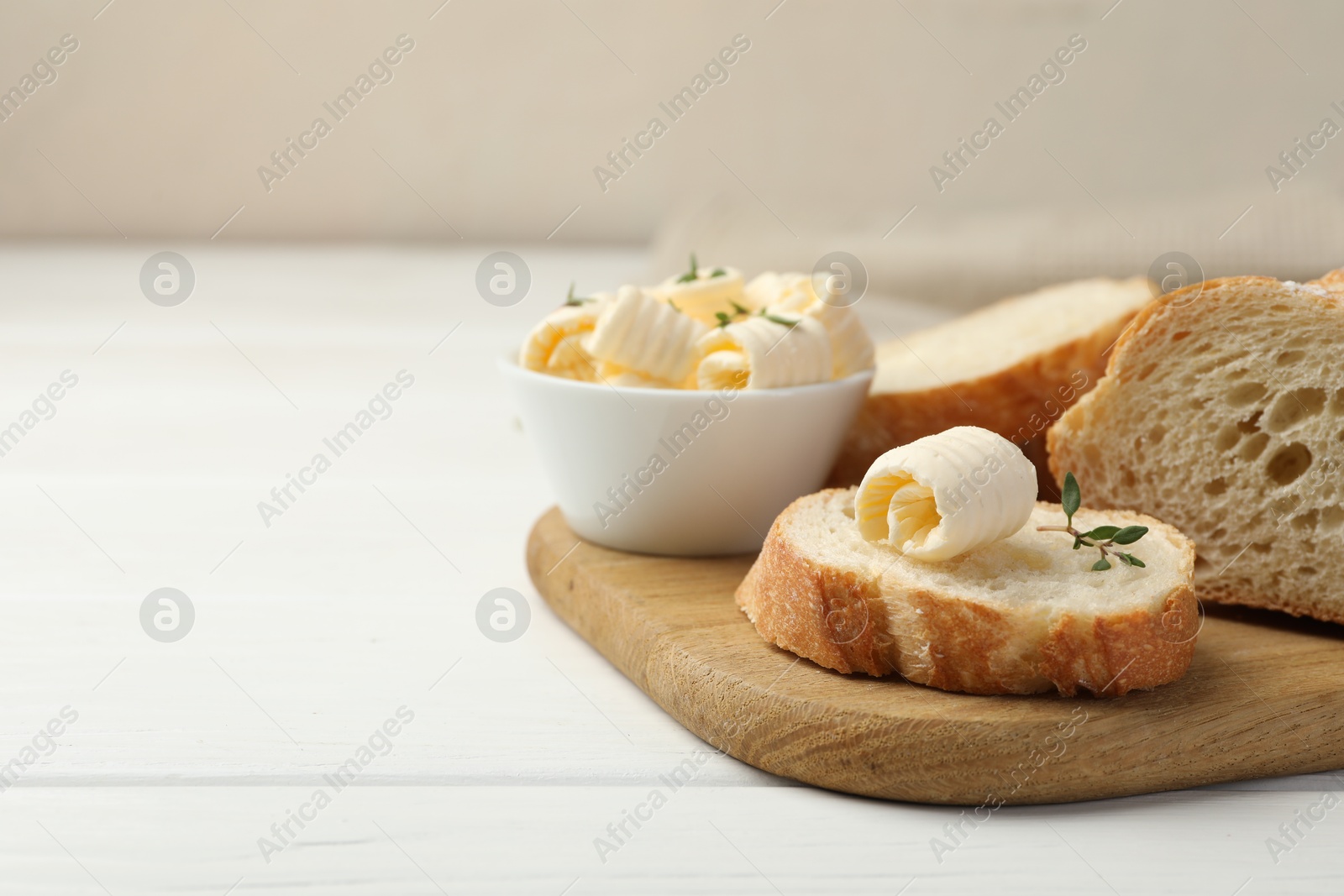 Photo of Cut baguette with butter and herbs on white wooden table, closeup. Space for text