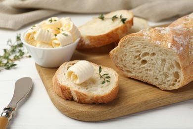 Photo of Cut baguette with butter and herbs on white wooden table, closeup