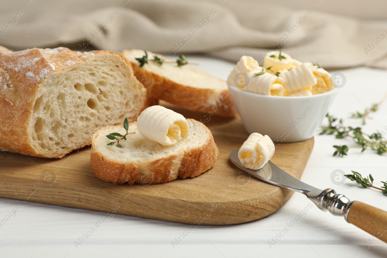 Photo of Cut baguette with butter and herbs on white wooden table, closeup